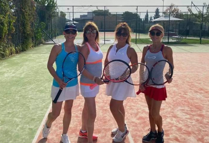 4 women on a tennis court holding rackets