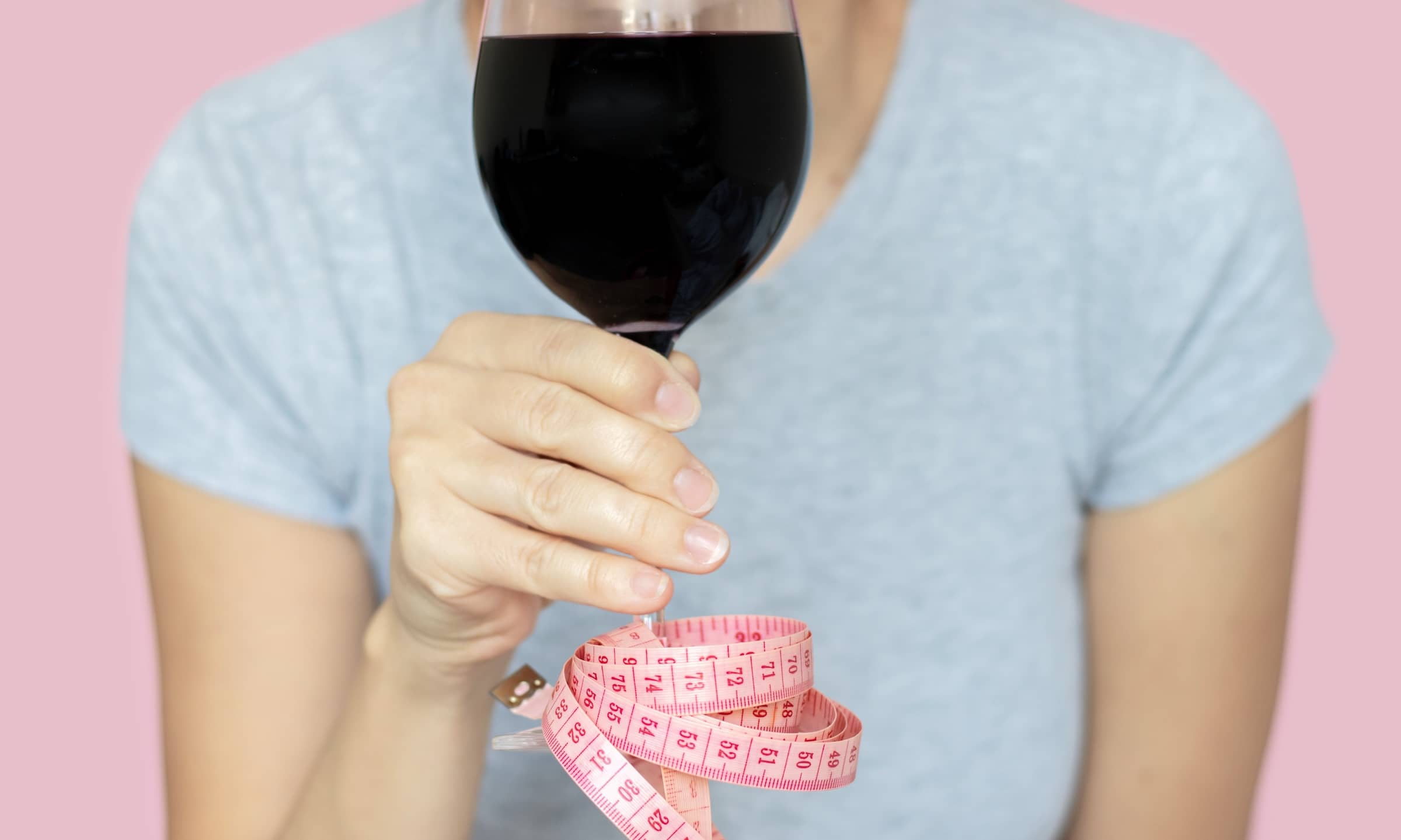 slim woman holding glass with red wine in hand measure tape attached by foot base